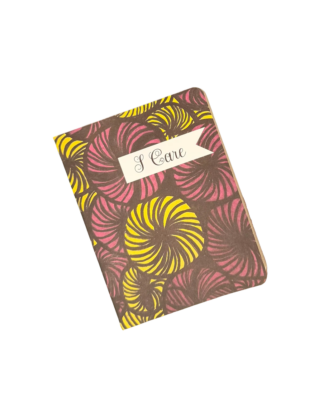 A hardcover notebook with a retro floral pattern in pink, yellow, and brown, featuring a white paper banner on the cover that reads 'I Care'. The notebook is placed diagonally on a brown wooden surface.